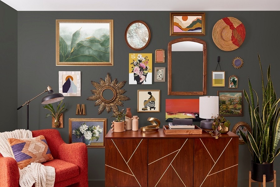 Living room with a dark accent wall, framed art, and mirrors hung with Command Strips. A wooden sideboard, red armchair, and tall plant complete the chic decor.
