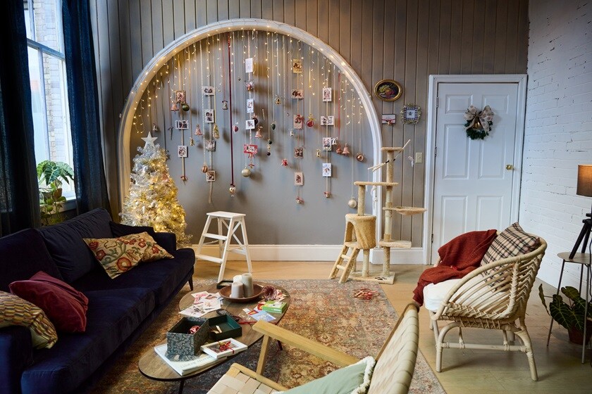 Living room with Christmas décor hanging from an arch using Command Hooks, a lit white tree, dark sofa, central coffee table, and a cat tower.
