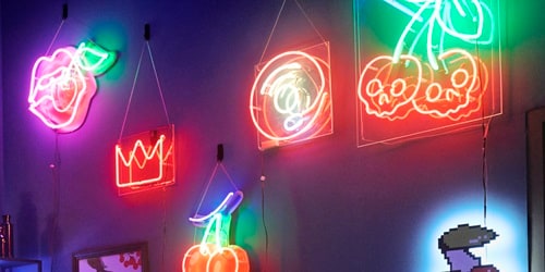 A dark room is lit up with red and green neon lights shaped as cherries, lips and a crown - hung on the wall with Command hooks.

