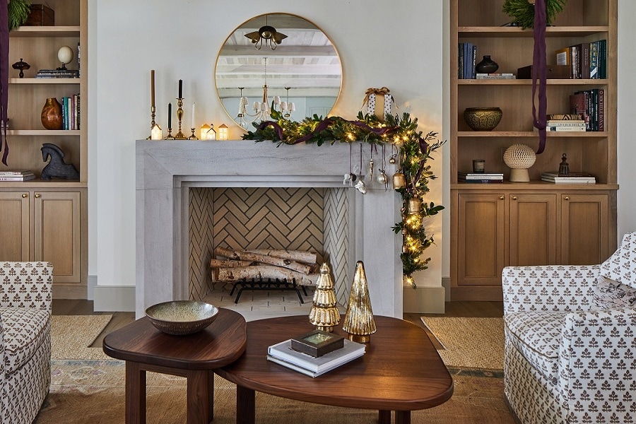 Living room with a herringbone fireplace, decorated mantel, and round mirror. With Christmas decorations hung with Command hooks for a cozy setting.
